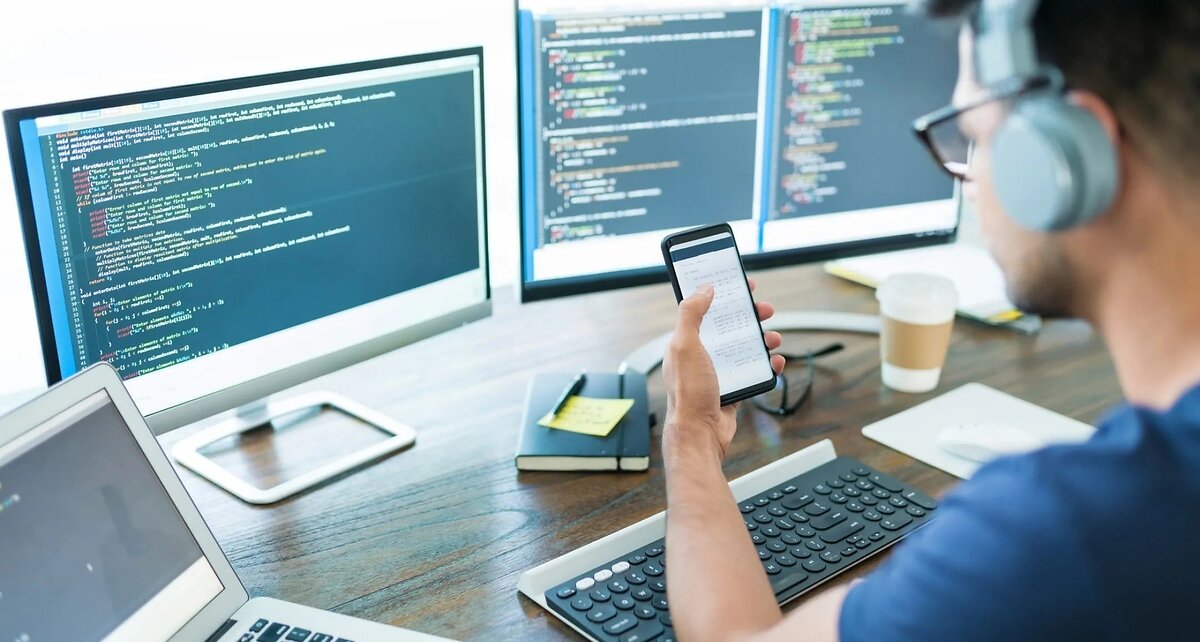 Man Viewing Code On Mobile With Screens Behind